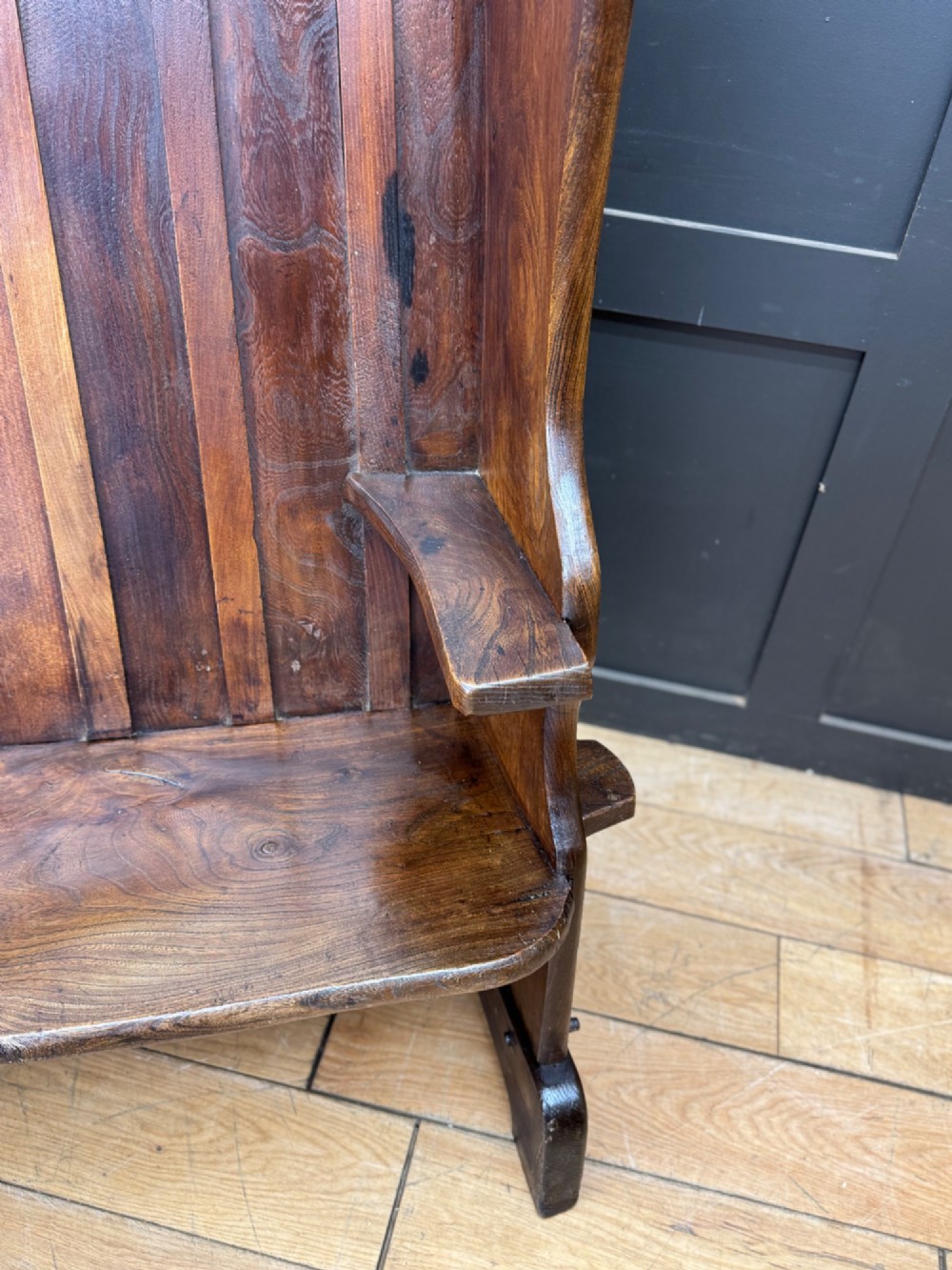 A curved antique elm wooden settle pew featuring a slatted high back, shaped side wings, and visible pegged joinery. View IV