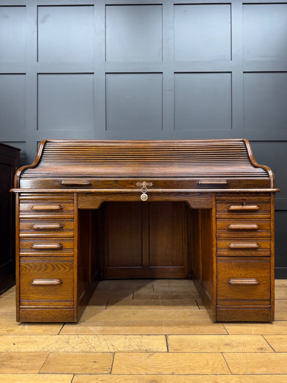 An Edwardian oak roll top pedestal desk featuring a flexible wooden tambour cover and twin drawer pedestals with carved handles.