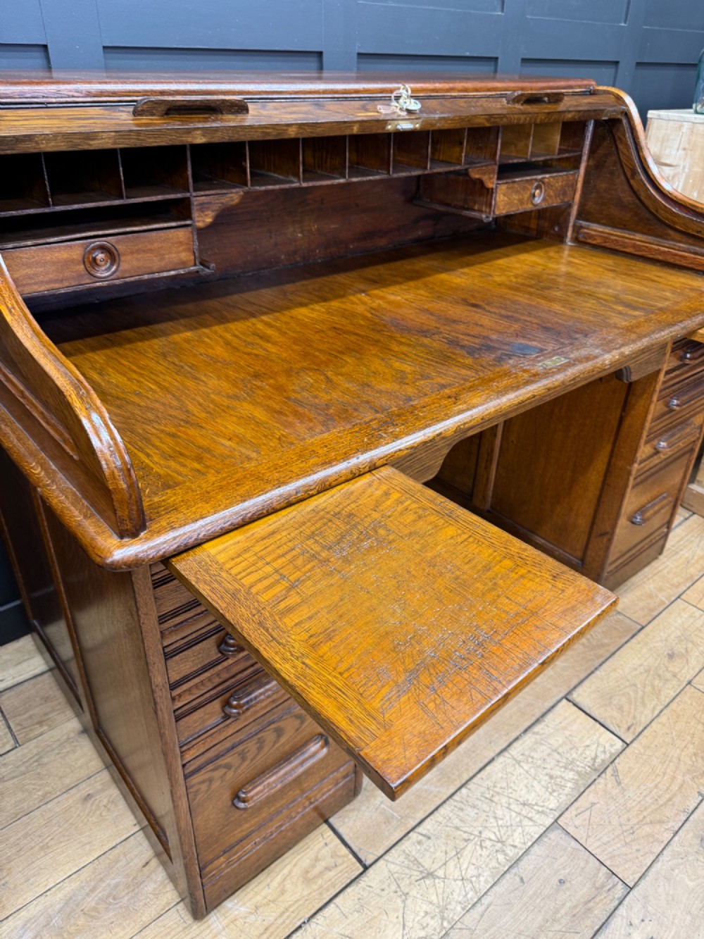 An Edwardian oak roll top pedestal desk featuring a flexible wooden tambour cover and twin drawer pedestals with carved handles. View VI