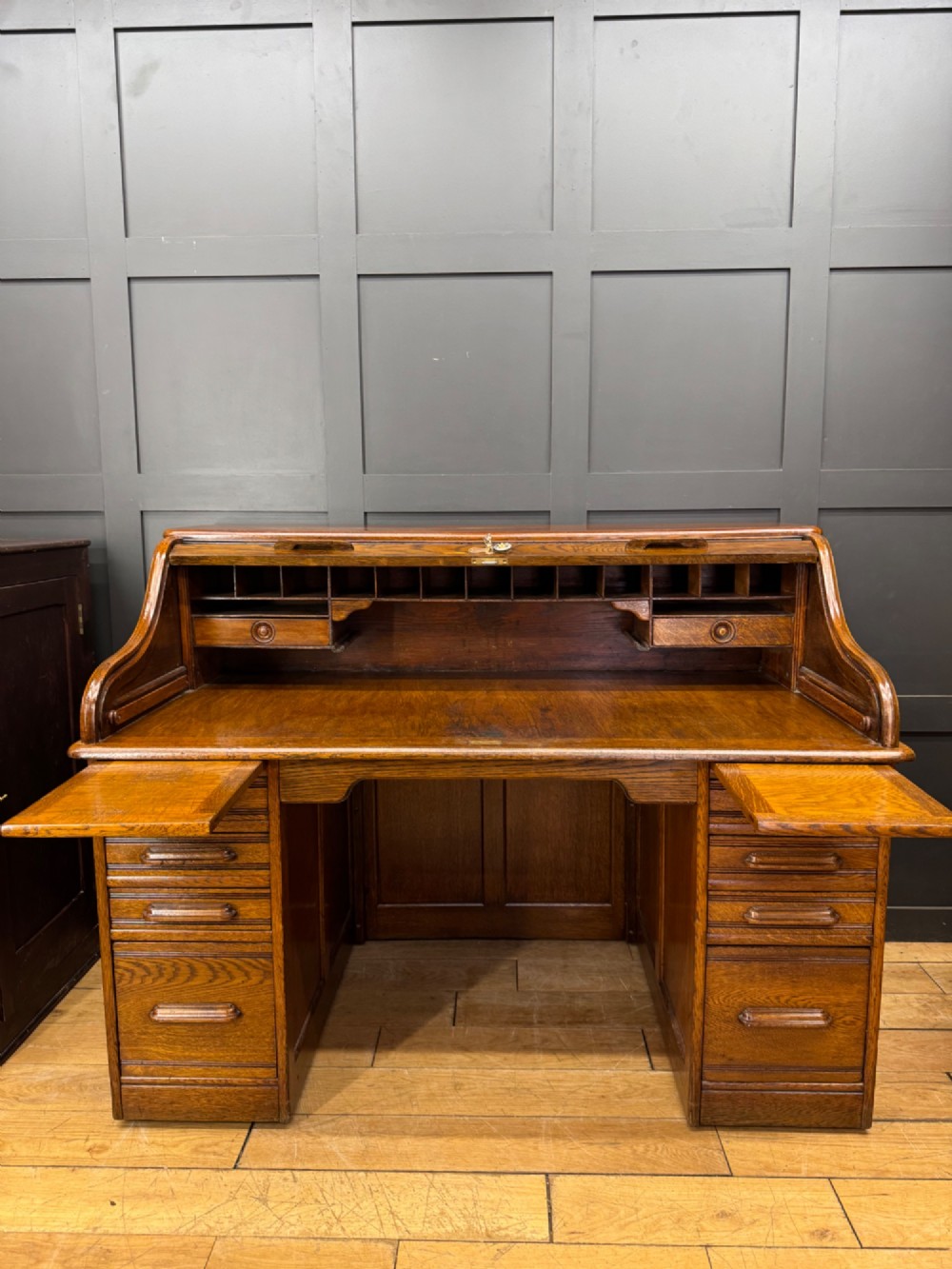 An Edwardian oak roll top pedestal desk featuring a flexible wooden tambour cover and twin drawer pedestals with carved handles. View VII