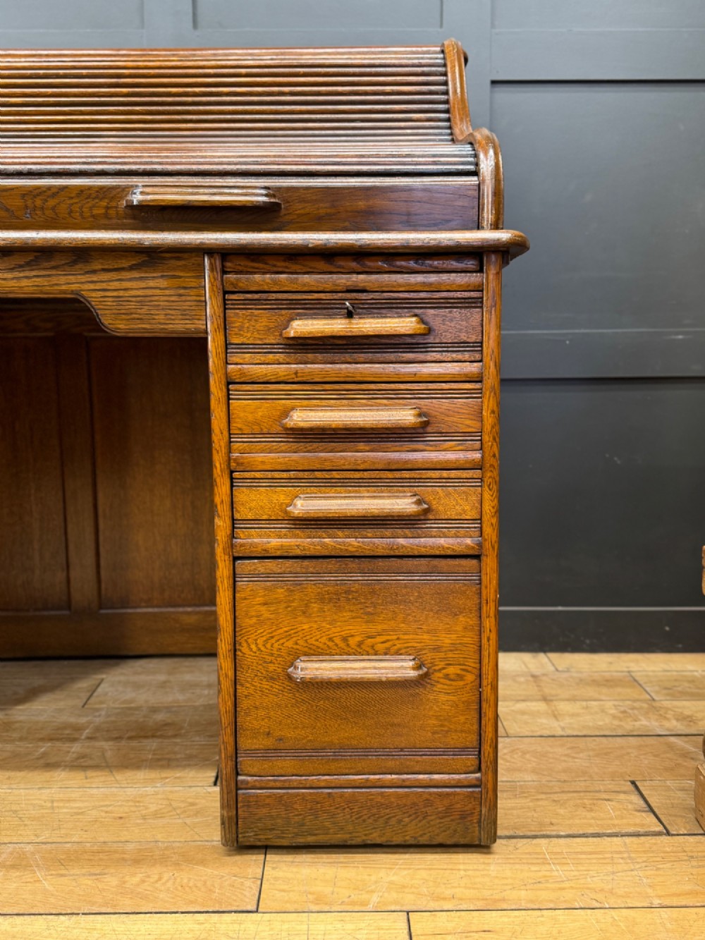 An Edwardian oak roll top pedestal desk featuring a flexible wooden tambour cover and twin drawer pedestals with carved handles. View X