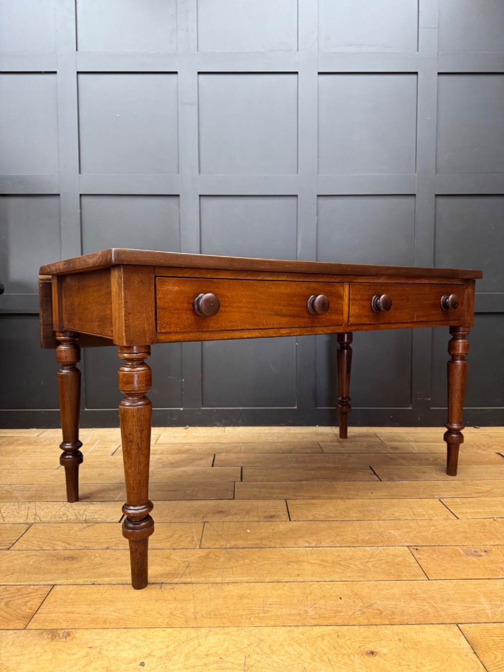 A Victorian mahogany writing table featuring two front drawers with wooden turned knobs, four turned legs, and a drop-leaf panel.