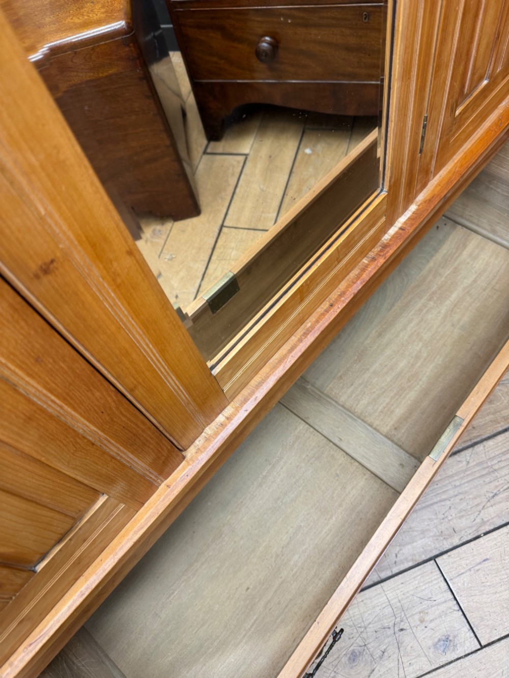 A tall Edwardian satinwood wardrobe featuring a central mirrored door, panelled side doors, a carved rosette frieze, and a wide drawer at the base. View VI