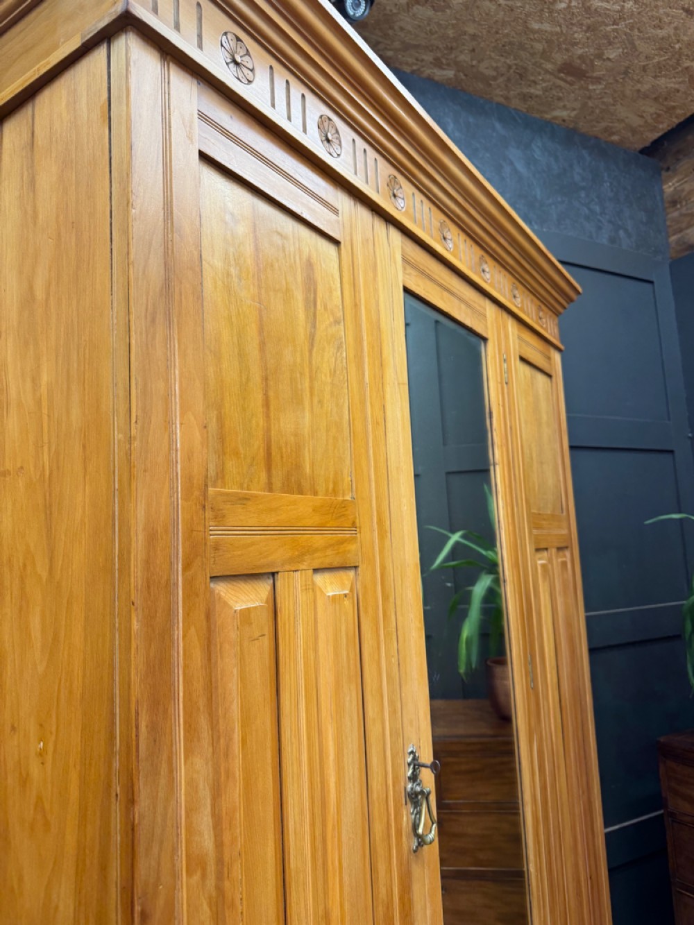 A tall Edwardian satinwood wardrobe featuring a central mirrored door, panelled side doors, a carved rosette frieze, and a wide drawer at the base. View VII