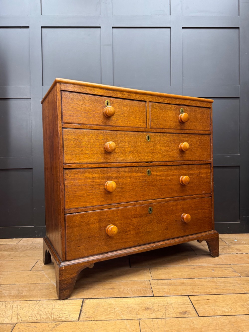 An antique oak chest of drawers featuring two short drawers above three long graduating drawers, complete with turned wooden knobs and bracket feet.