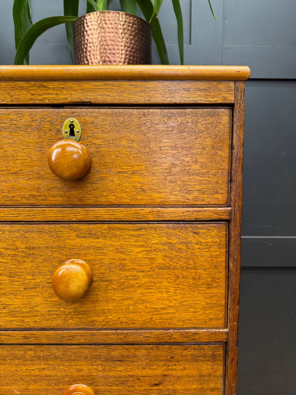 An antique oak chest of drawers featuring two short drawers above three long graduating drawers, complete with turned wooden knobs and bracket feet. View V