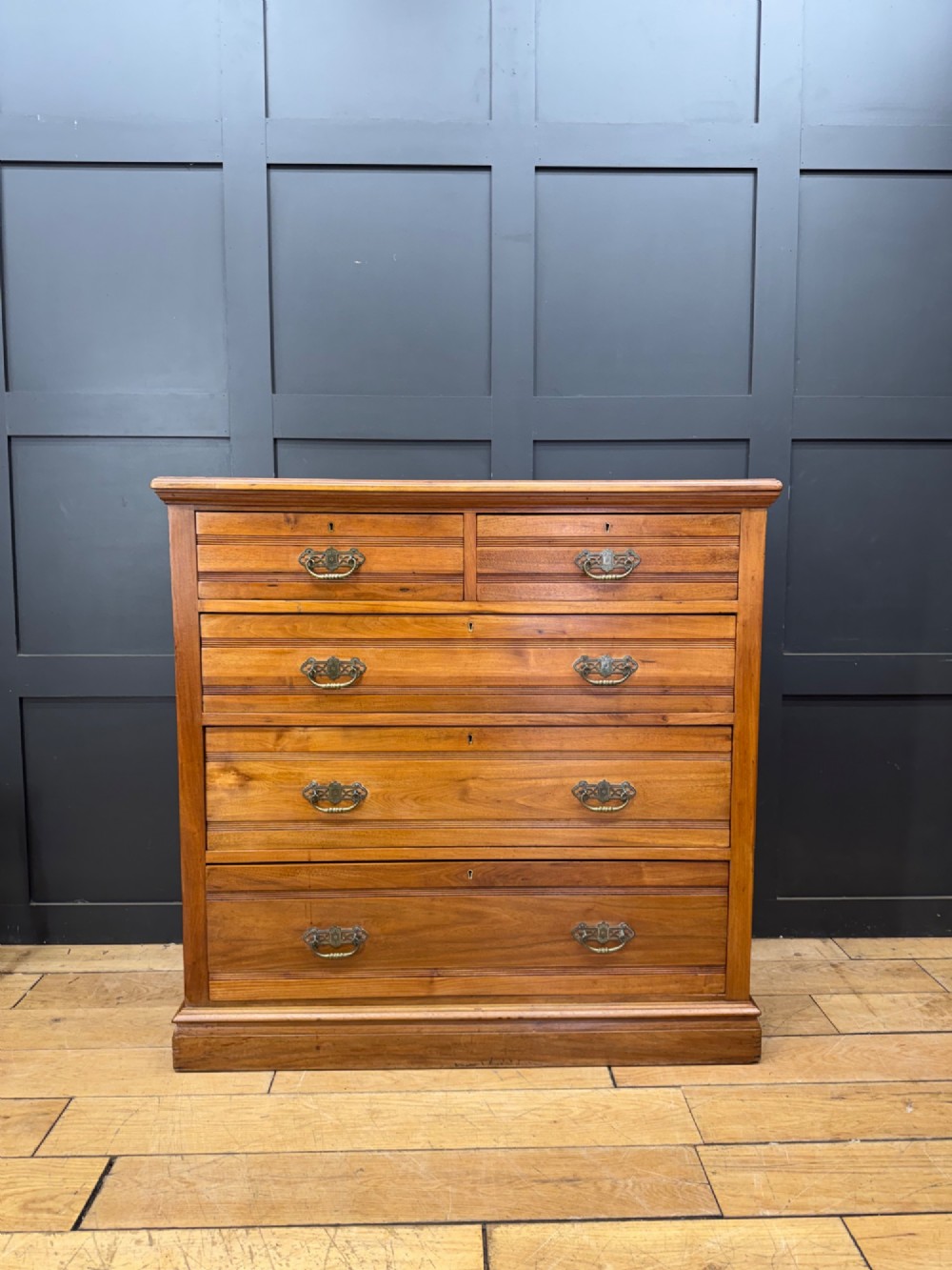 A Victorian antique walnut chest featuring two short over three long drawers with ornate brass handles and reeded drawer fronts resting on a solid plinth base.