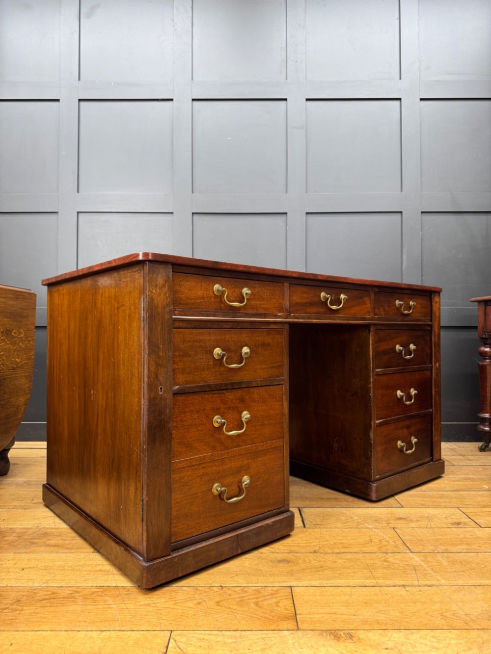 An antique mahogany pedestal desk featuring three frieze drawers, twin drawer pedestals with brass drop handles, and a solid plinth base.