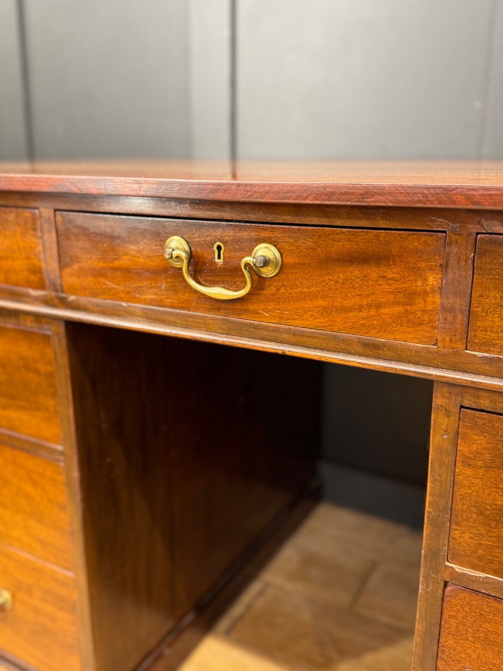 An antique mahogany pedestal desk featuring three frieze drawers, twin drawer pedestals with brass drop handles, and a solid plinth base. View V