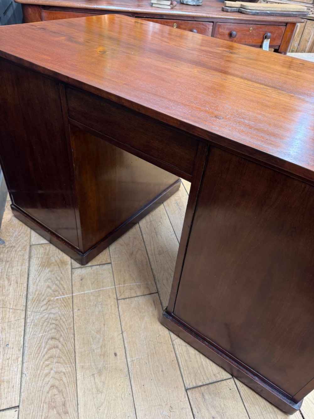An antique mahogany pedestal desk featuring three frieze drawers, twin drawer pedestals with brass drop handles, and a solid plinth base. View VII