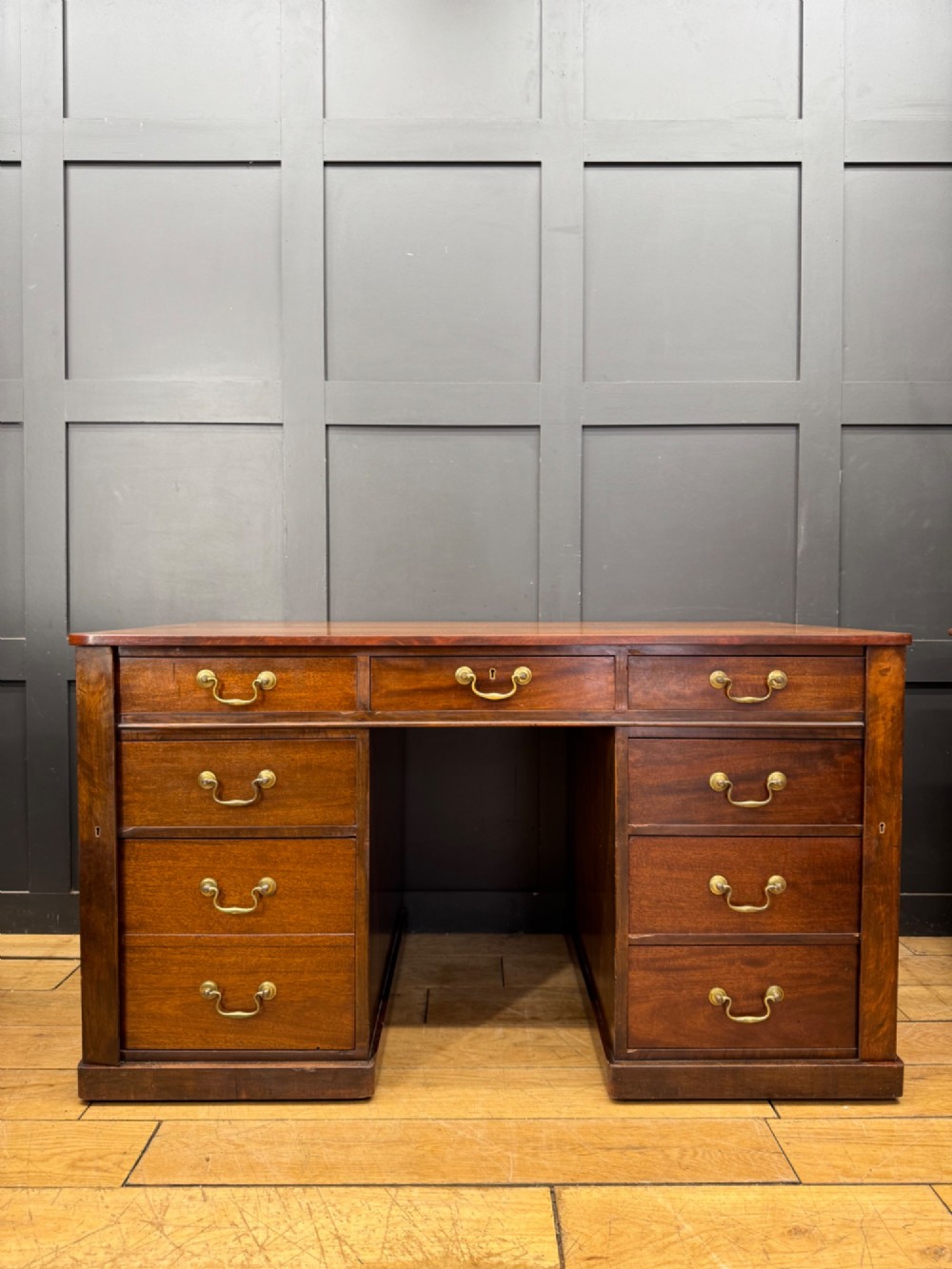 An antique mahogany pedestal desk featuring three frieze drawers, twin drawer pedestals with brass drop handles, and a solid plinth base. View VIII
