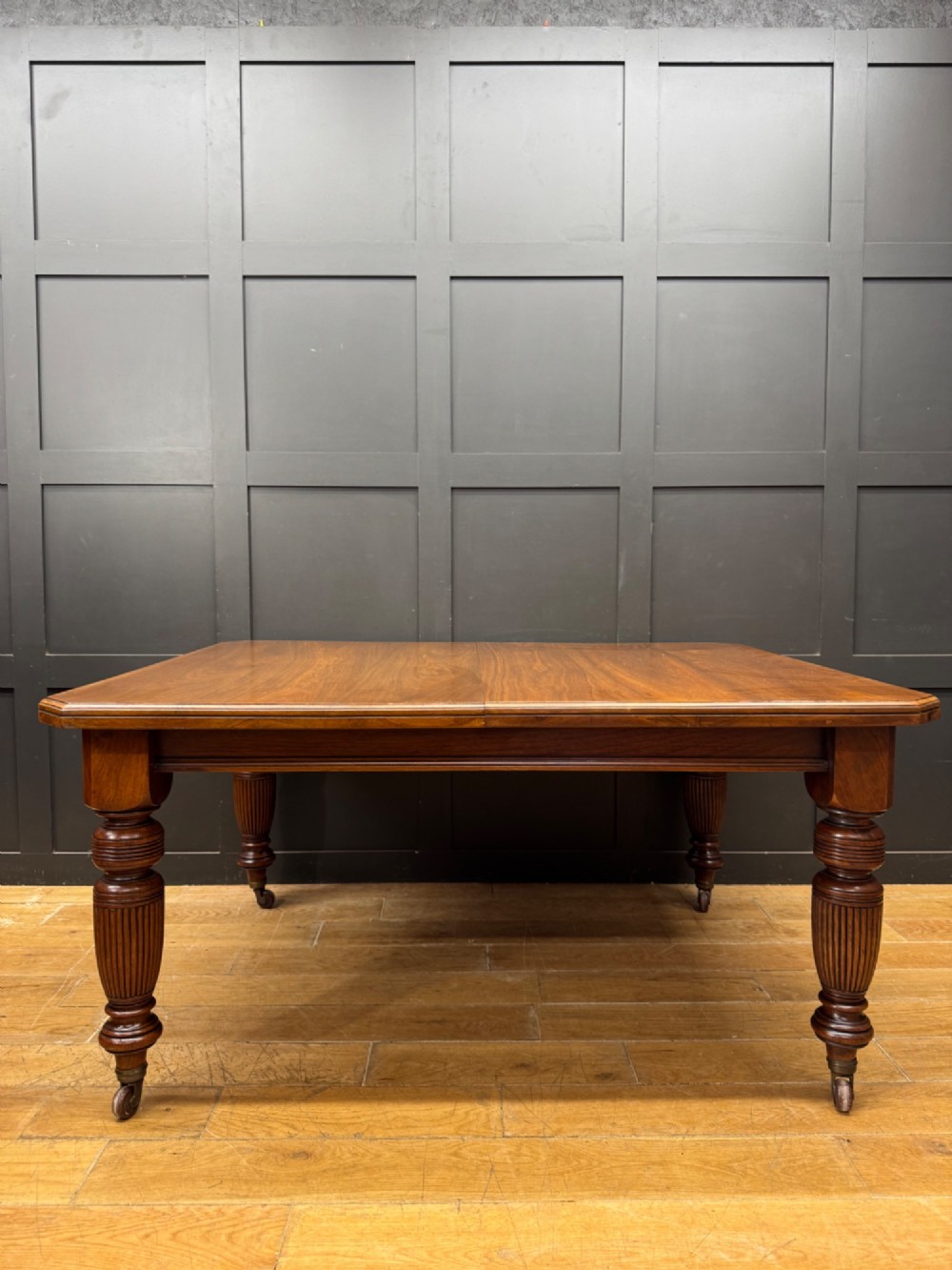 A solid walnut Victorian extending dining table with reeded turned legs set on brass castors. View II