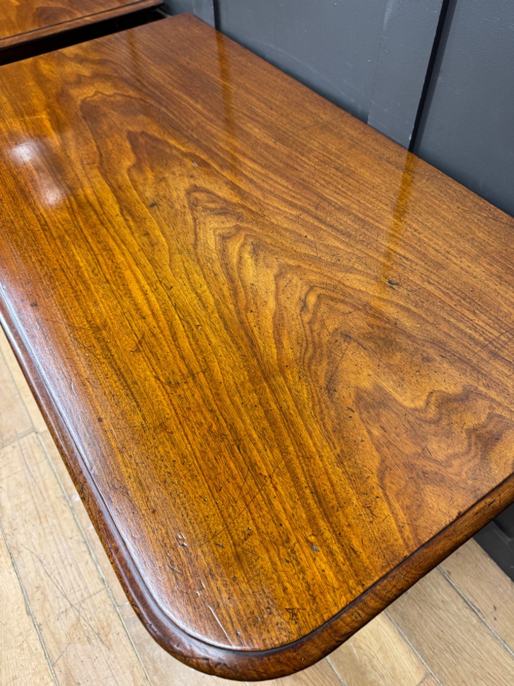 A matching pair of dark mahogany side tables featuring turned legs and brass castors standing against a panelled wall. View II