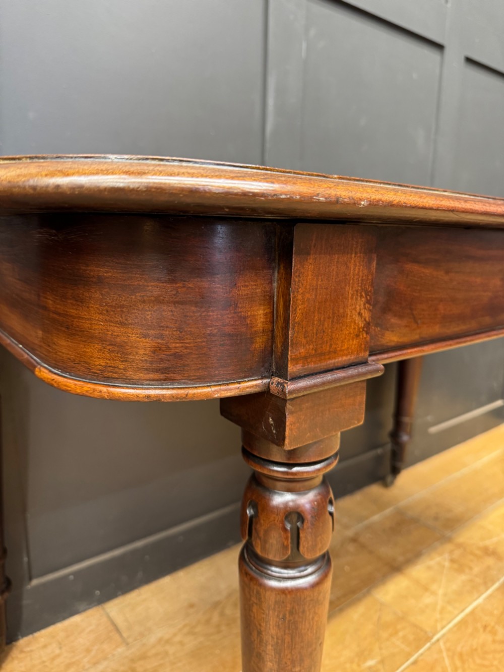 A matching pair of dark mahogany side tables featuring turned legs and brass castors standing against a panelled wall. View V