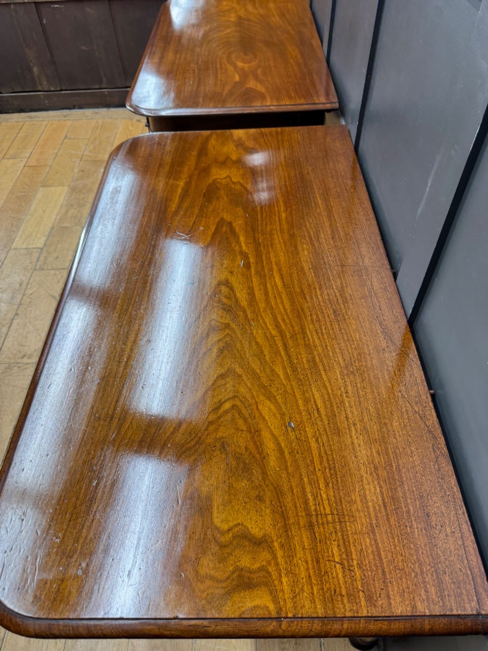 A matching pair of dark mahogany side tables featuring turned legs and brass castors standing against a panelled wall. View VI