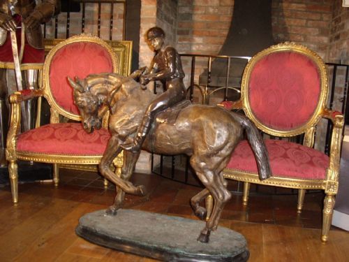 fig 1. A large patinated bronze sculpture depicting a jockey wearing riding attire mounted on a trotting racehorse, set upon an integrated oval bronze base.