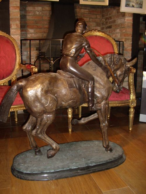fig 2. A large patinated bronze sculpture depicting a jockey wearing riding attire mounted on a trotting racehorse, set upon an integrated oval bronze base.