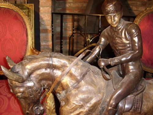 fig 3. A large patinated bronze sculpture depicting a jockey wearing riding attire mounted on a trotting racehorse, set upon an integrated oval bronze base.