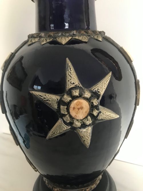 fig 2. A cobalt blue glazed terracotta vase adorned with applied silver metalwork, a star motif, bone inlays, and mounted on a dark circular pedestal.