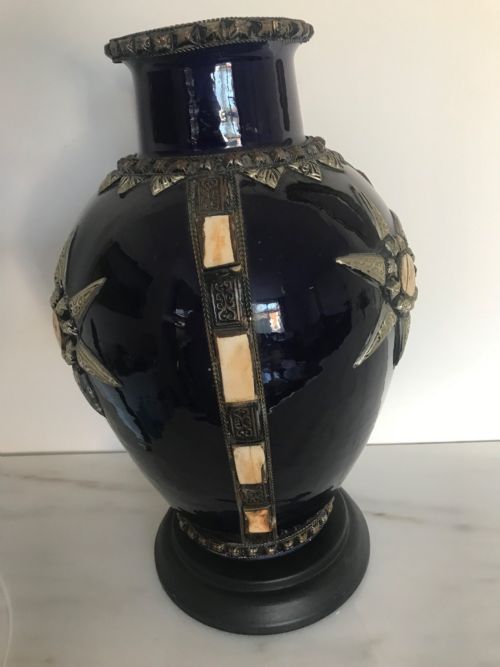 fig 5. A cobalt blue glazed terracotta vase adorned with applied silver metalwork, a star motif, bone inlays, and mounted on a dark circular pedestal.