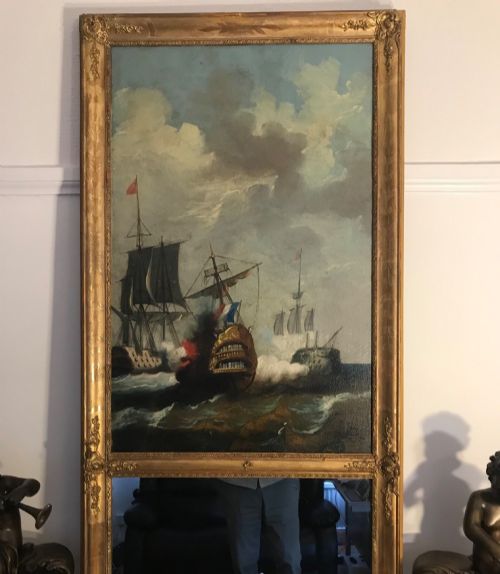 fig 2. A tall rectangular French trumeau mirror with a gilded frame containing an upper oil painting of a naval seascape and a lower mirror glass section.