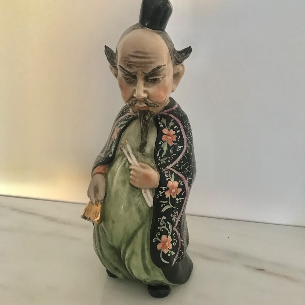 A Chinese ceramic figurine of a scholar wearing a black patterned robe and green garments, holding two scrolls and a small gold bell. View II