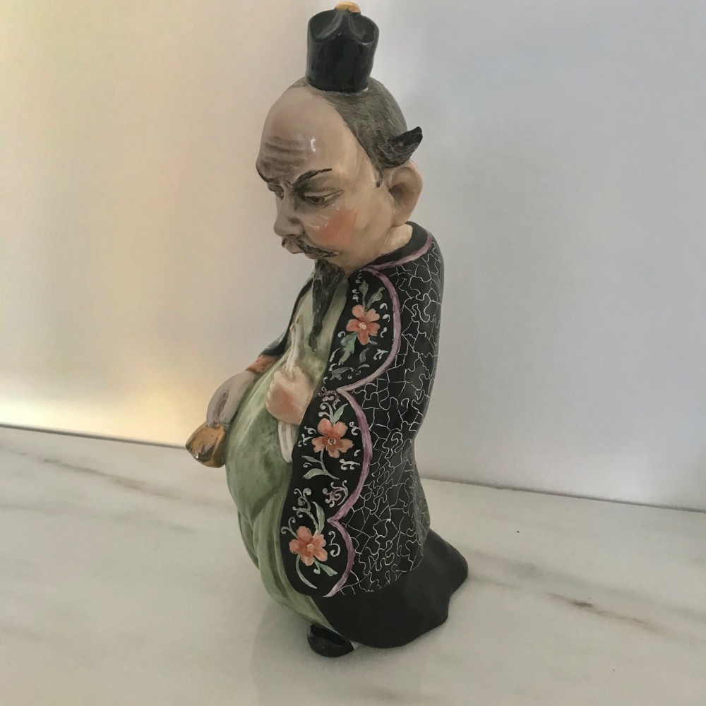 A Chinese ceramic figurine of a scholar wearing a black patterned robe and green garments, holding two scrolls and a small gold bell. View III
