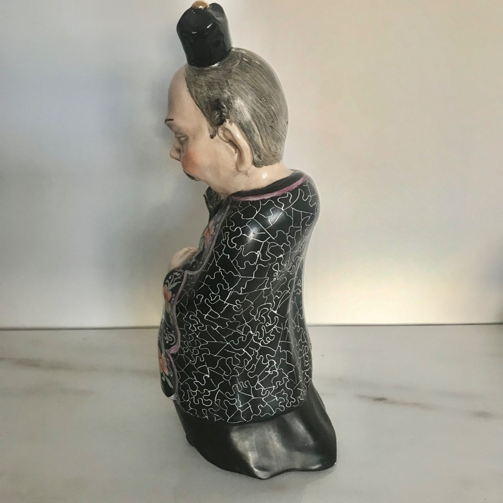 A Chinese ceramic figurine of a scholar wearing a black patterned robe and green garments, holding two scrolls and a small gold bell. View IV