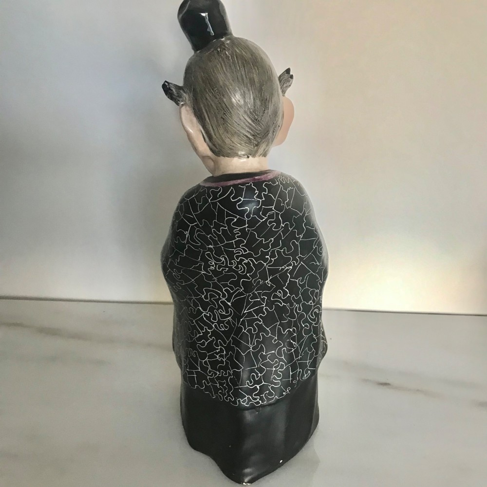 A Chinese ceramic figurine of a scholar wearing a black patterned robe and green garments, holding two scrolls and a small gold bell. View V