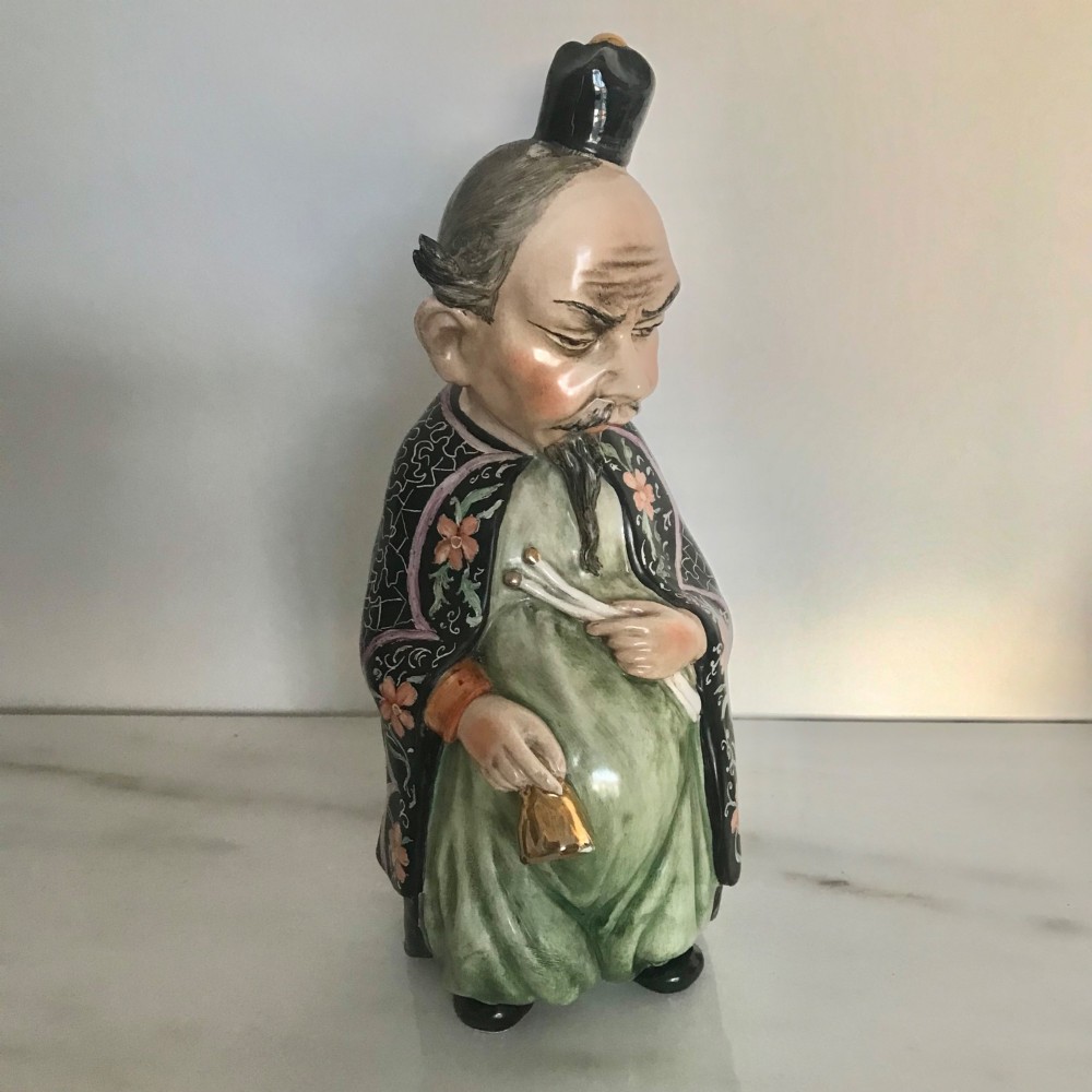 A Chinese ceramic figurine of a scholar wearing a black patterned robe and green garments, holding two scrolls and a small gold bell. View VIII