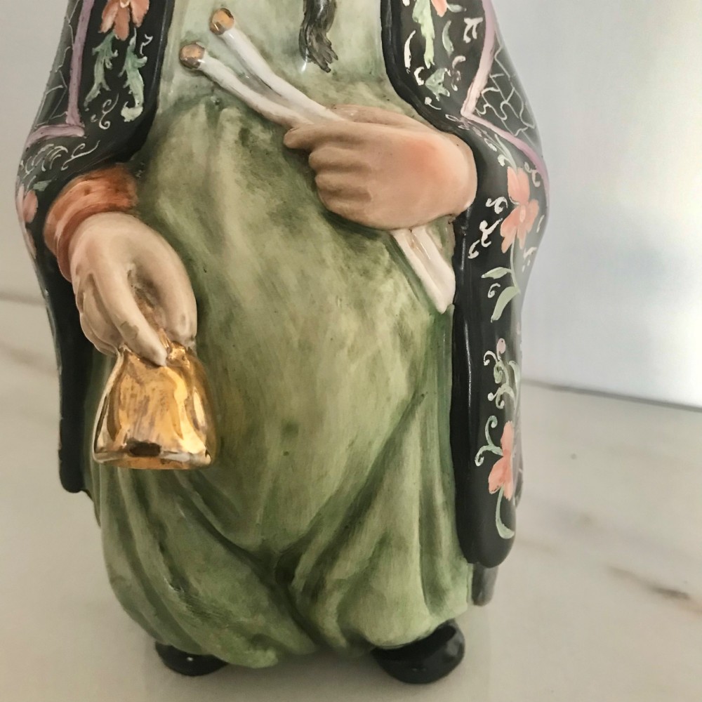 A Chinese ceramic figurine of a scholar wearing a black patterned robe and green garments, holding two scrolls and a small gold bell. View X