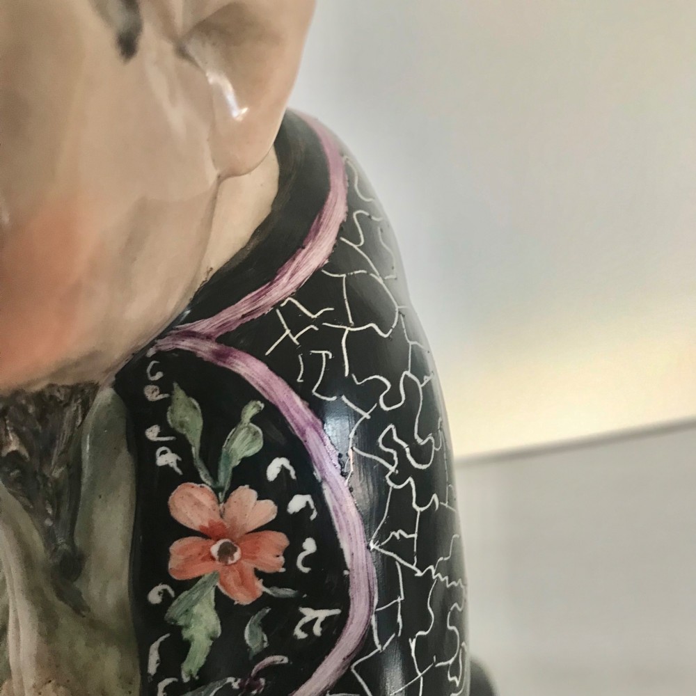 A Chinese ceramic figurine of a scholar wearing a black patterned robe and green garments, holding two scrolls and a small gold bell. View XII