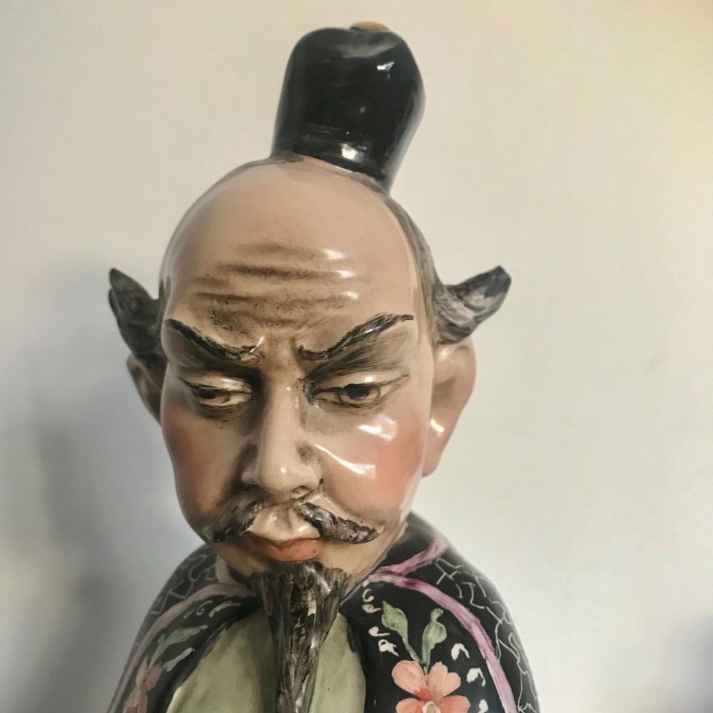 A Chinese ceramic figurine of a scholar wearing a black patterned robe and green garments, holding two scrolls and a small gold bell. View XIII