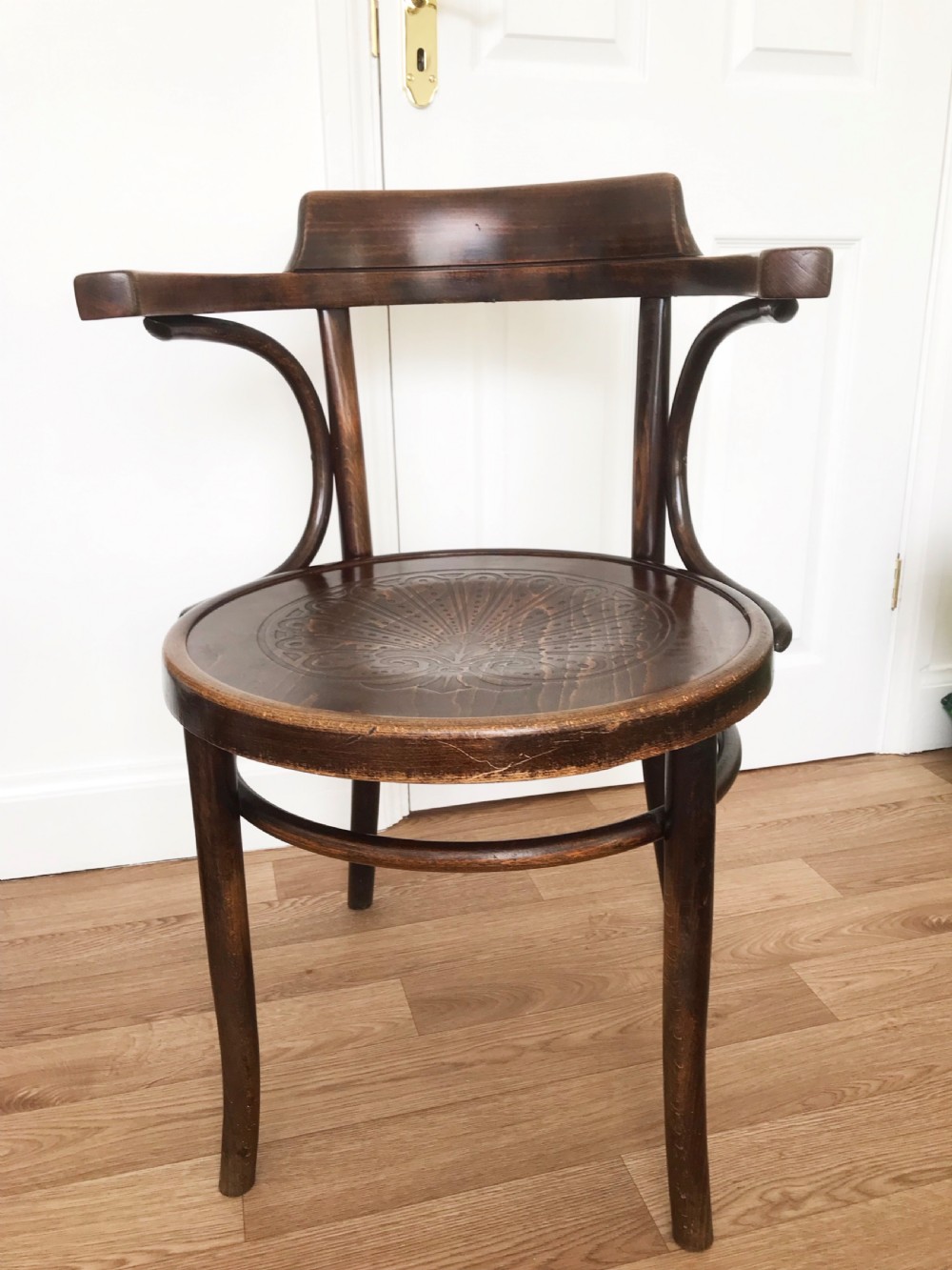 A dark brown stained bentwood carver chair featuring curved armrests, turned front legs, and an embossed circular wooden seat panel.