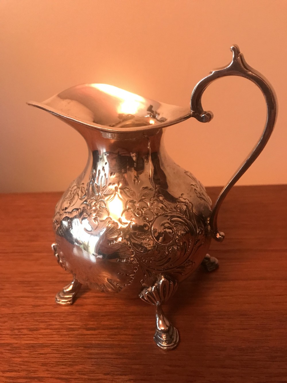 An Edwardian three-piece silver-plated tea set comprising a teapot, milk jug, and sugar bowl featuring floral chasing and scroll feet. View XVIII