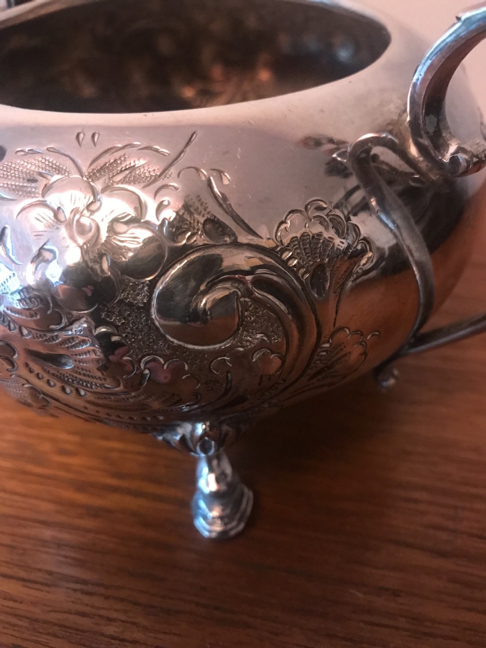 An Edwardian three-piece silver-plated tea set comprising a teapot, milk jug, and sugar bowl featuring floral chasing and scroll feet. View XIX