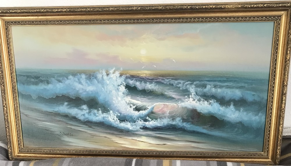 A framed horizontal oil painting depicting crashing ocean waves along a sandy shore during a pastel sunset, enclosed within an ornate gold frame.