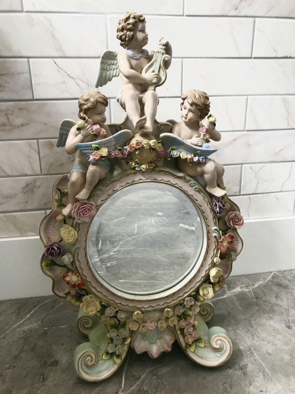 An ornate Continental porcelain table mirror featuring sculpted winged cherubs and hand-modelled floral encrustations around a circular mirror frame. View XXII