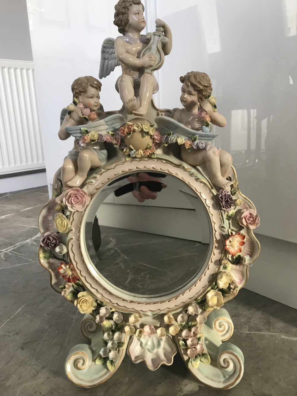 An ornate Continental porcelain table mirror featuring sculpted winged cherubs and hand-modelled floral encrustations around a circular mirror frame. View XXIV