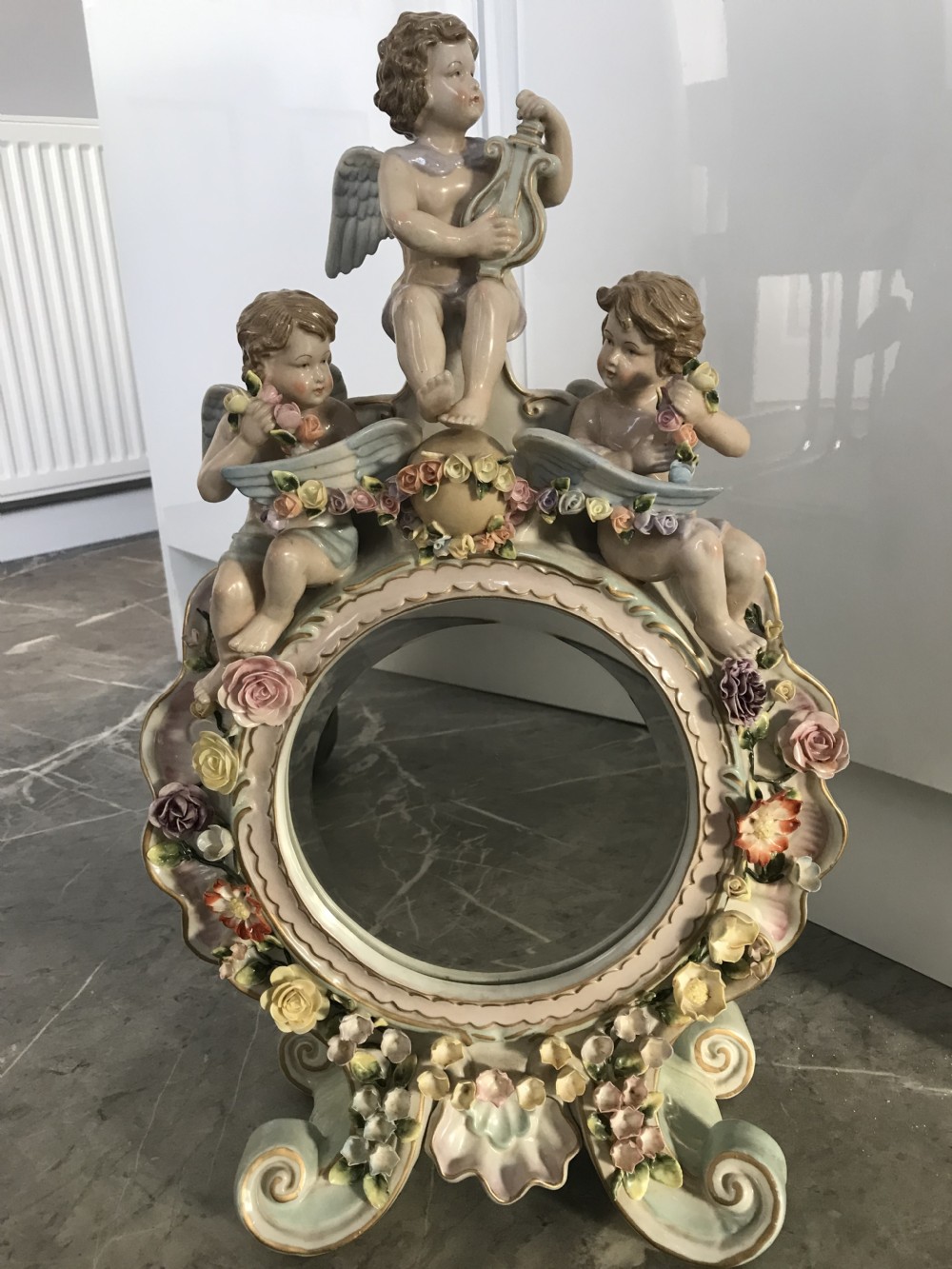 An ornate Continental porcelain table mirror featuring sculpted winged cherubs and hand-modelled floral encrustations around a circular mirror frame.