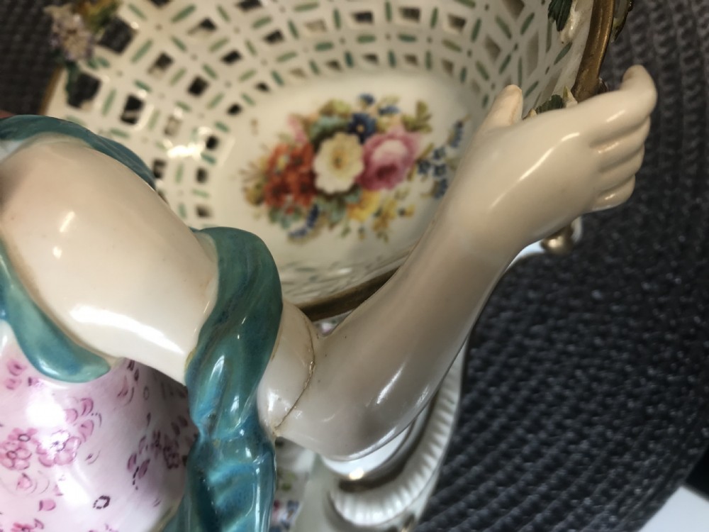 An 18th-century porcelain sweetmeat dish featuring a reclining female figure beside an openwork lattice basket adorned with hand-painted polychrome flowers and gilt trim. View XX