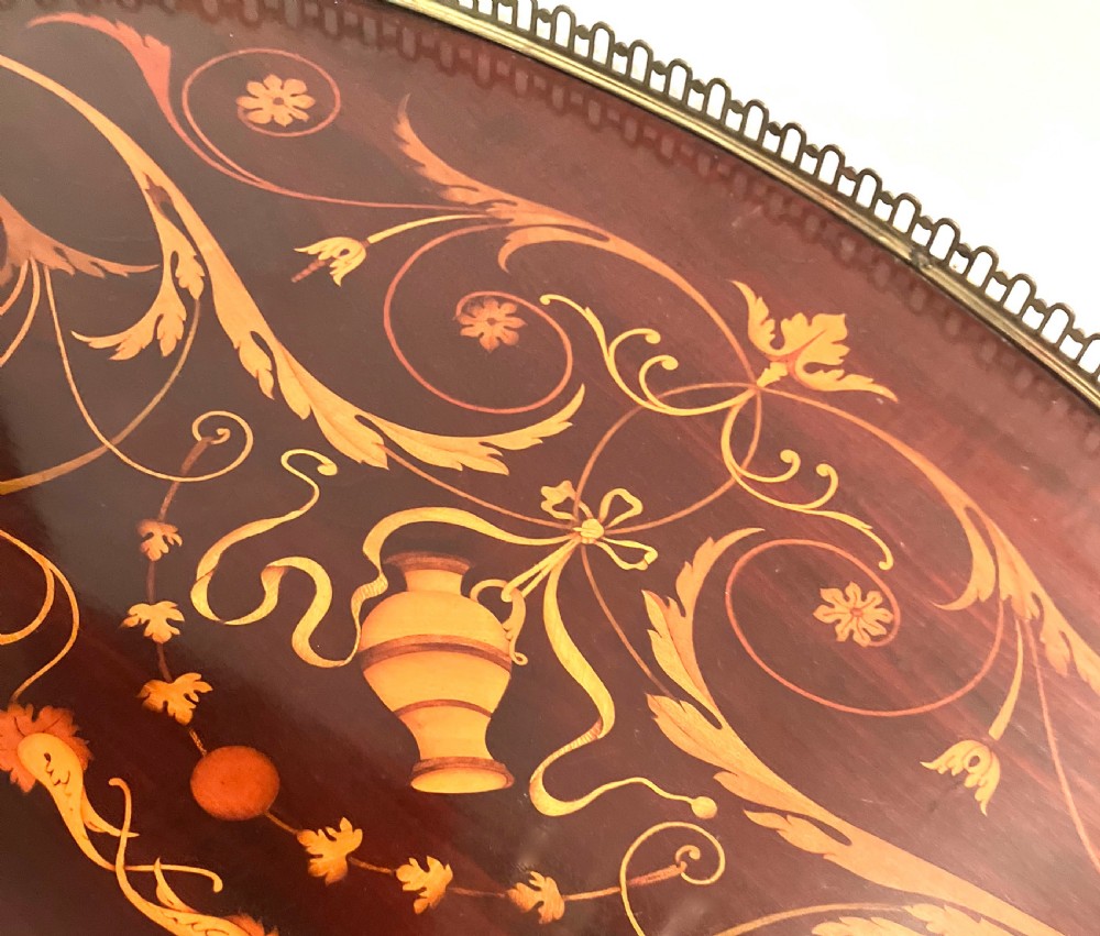 A crescent-shaped mahogany tray featuring inlaid botanical marquetry, a central urn motif, and a pierced brass gallery rim with handles. View V