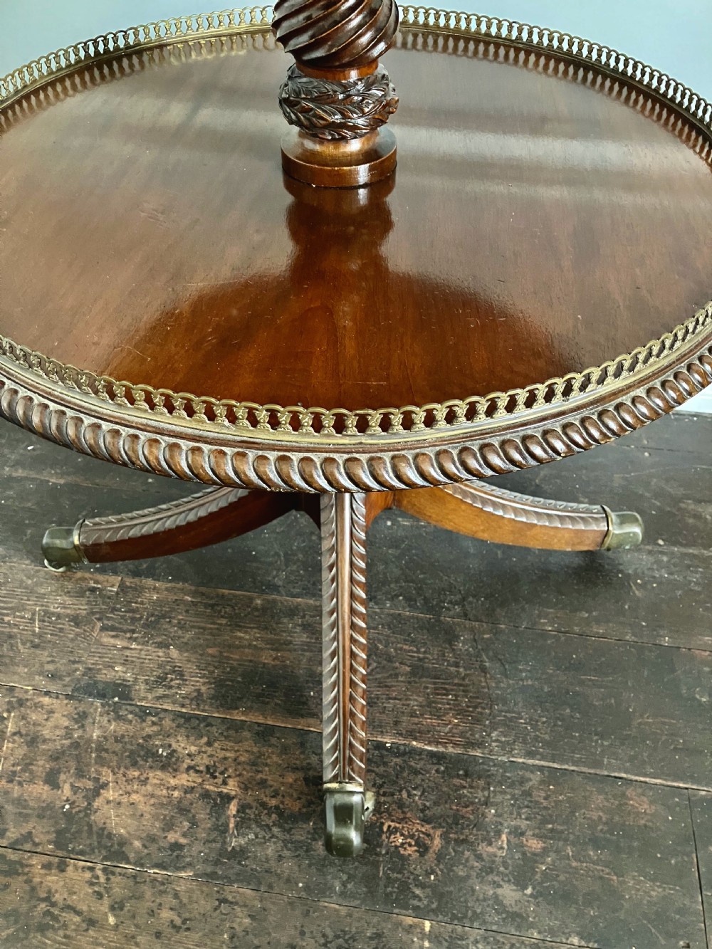 A three-tiered dark mahogany dumbwaiter table featuring pierced brass gallery rims, spiral-carved central supports, and splayed quadruped legs with brass castors. View IV