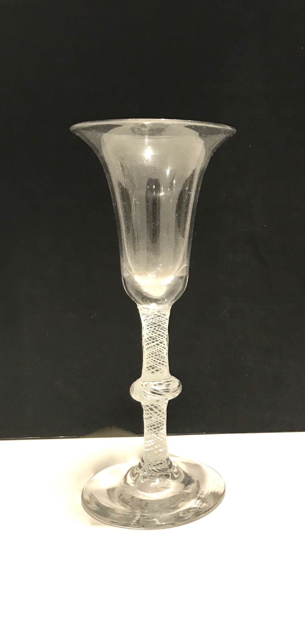 An 18th-century English glass featuring a bell-shaped bowl, a knopped opaque twist stem, and a wide circular foot.