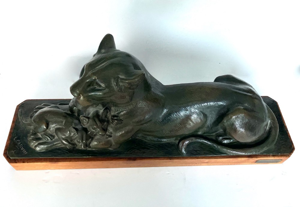 A dark patinated bronze sculpture depicting a reclining lioness alongside two cubs, mounted on a rectangular timber plinth. View IV