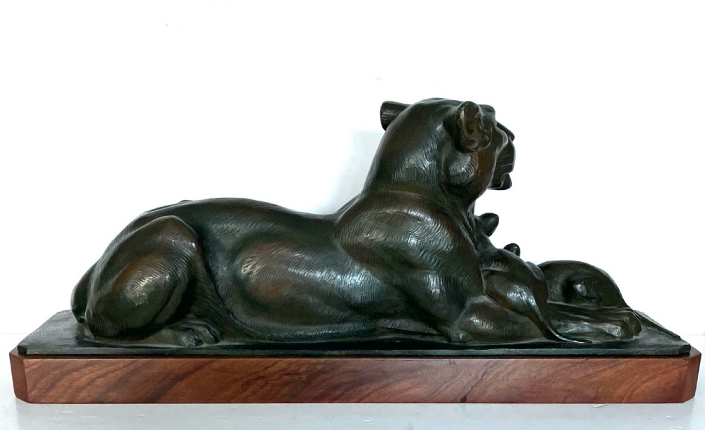 A dark patinated bronze sculpture depicting a reclining lioness alongside two cubs, mounted on a rectangular timber plinth. View VI