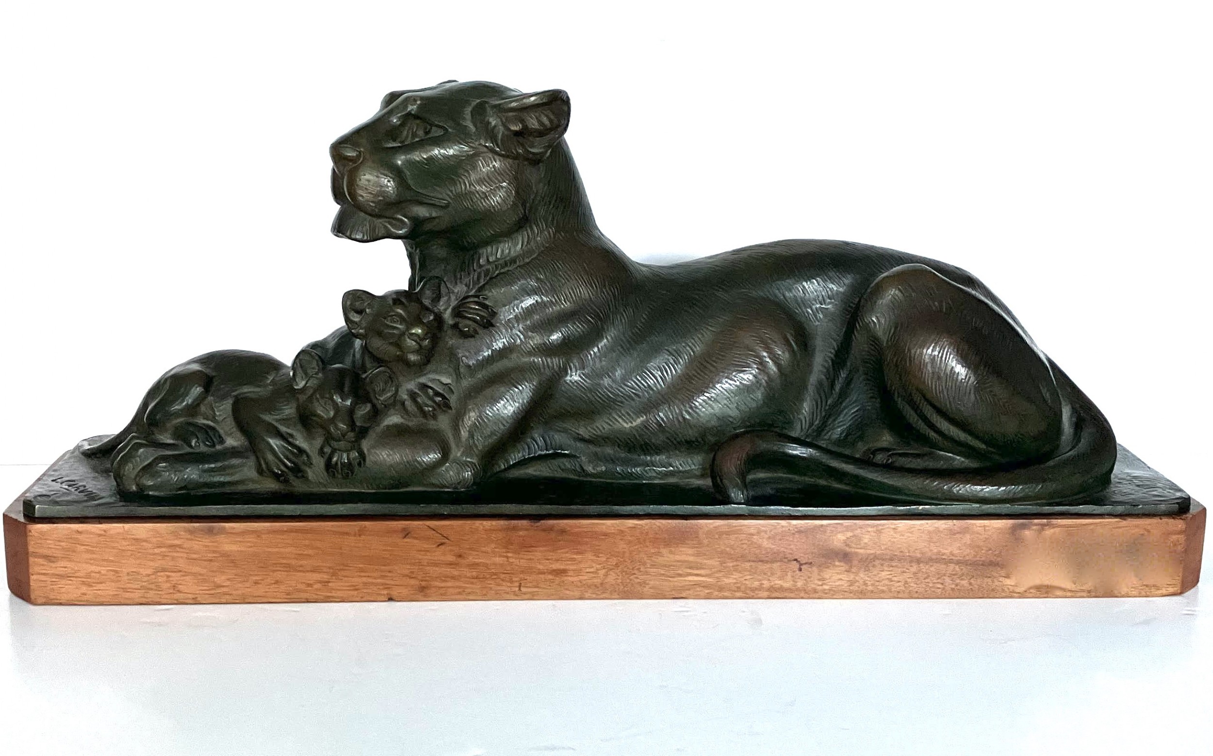 A dark patinated bronze sculpture depicting a reclining lioness alongside two cubs, mounted on a rectangular timber plinth.