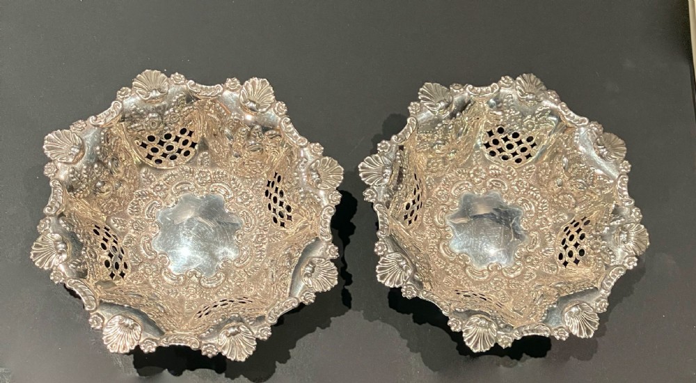 A pair of ornate Victorian silver bonbon dishes featuring delicate pierced openwork sides, repousse scrolling, and scalloped shell borders.