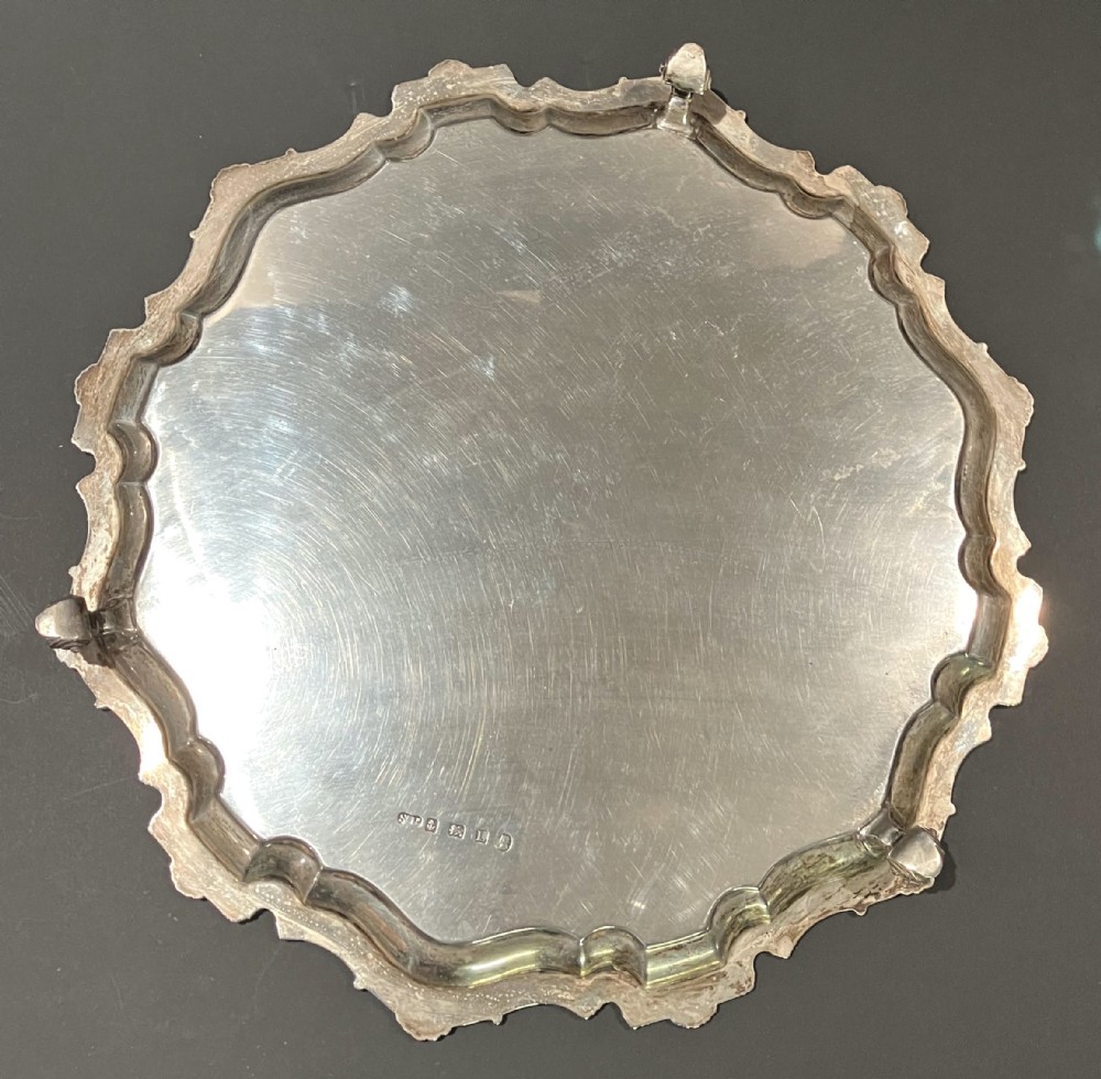 A circular hallmarked sterling silver salver with a shaped piecrust rim resting on cast feet.