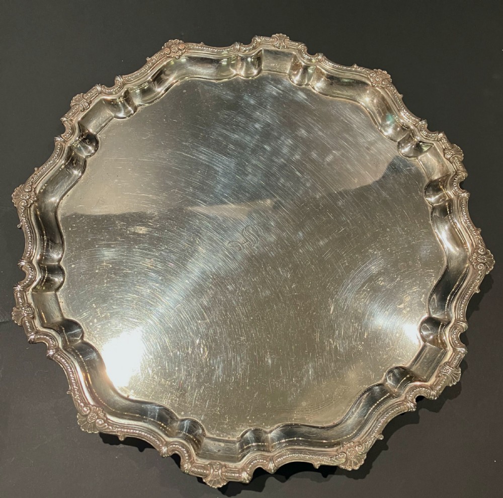 A circular hallmarked sterling silver salver with a shaped piecrust rim resting on cast feet. View II